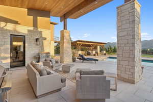 Expansive stone patio featuring a built-in outdoor kitchen area, a swimming pool, and a dedicated pergola structure