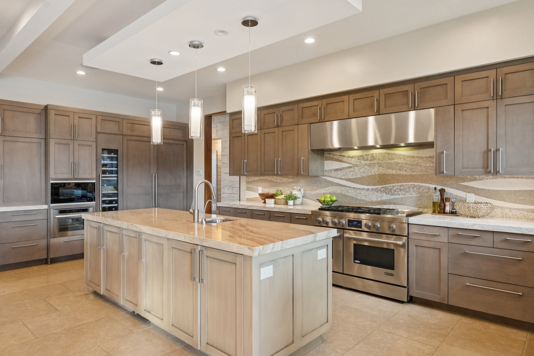 Gourmet kitchen featuring a large central island with a sink, stainless steel appliances, extensive cabinetry, a wine refrigerator, and a decorative tile backsplash