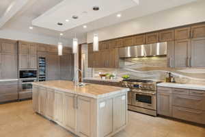 Gourmet kitchen featuring a large central island with a sink, stainless steel appliances, extensive cabinetry, a wine refrigerator, and a decorative tile backsplash