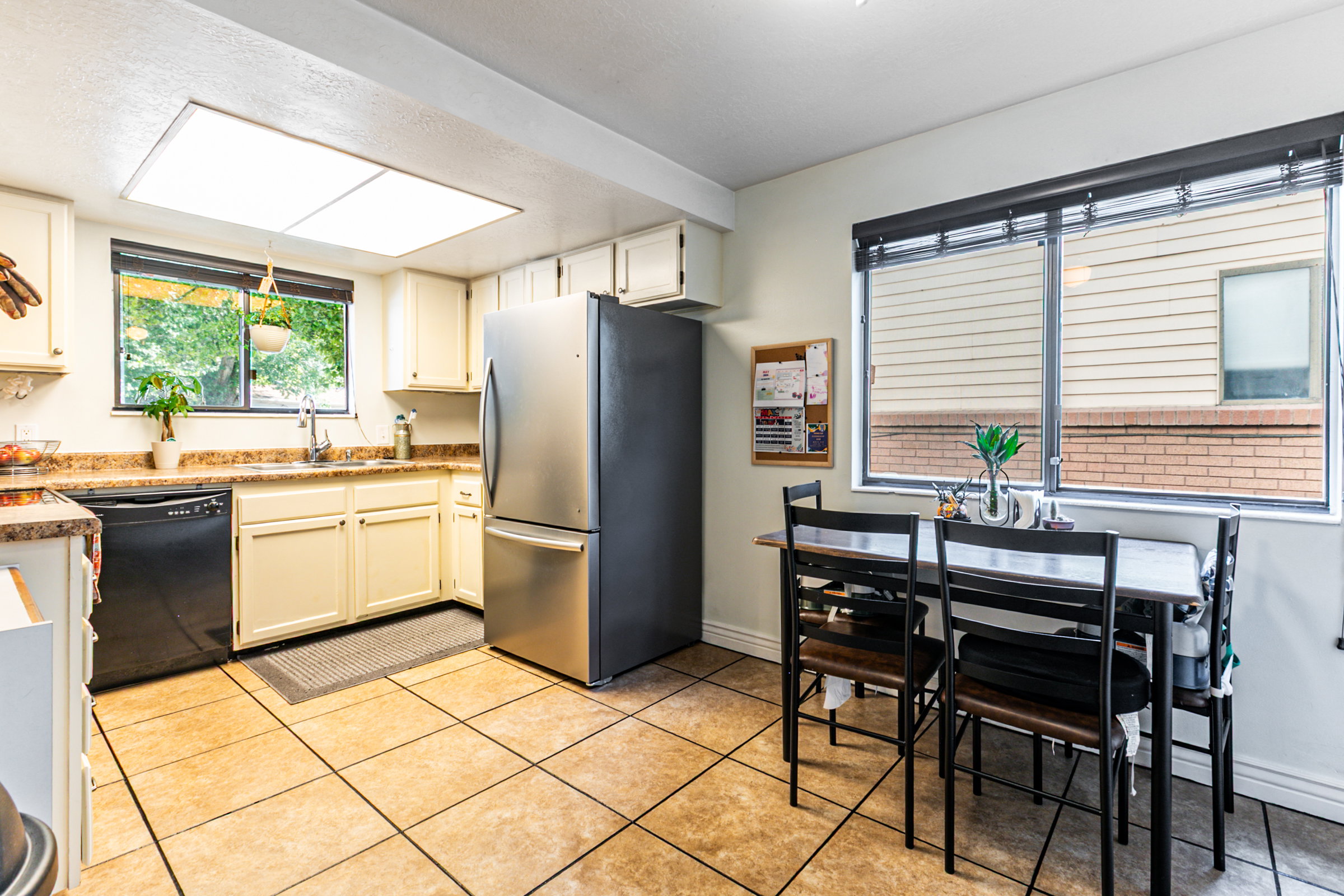 Kitchen featuring light-toned cabinetry, a stainless steel refrigerator, black dishwasher, and tiled flooring