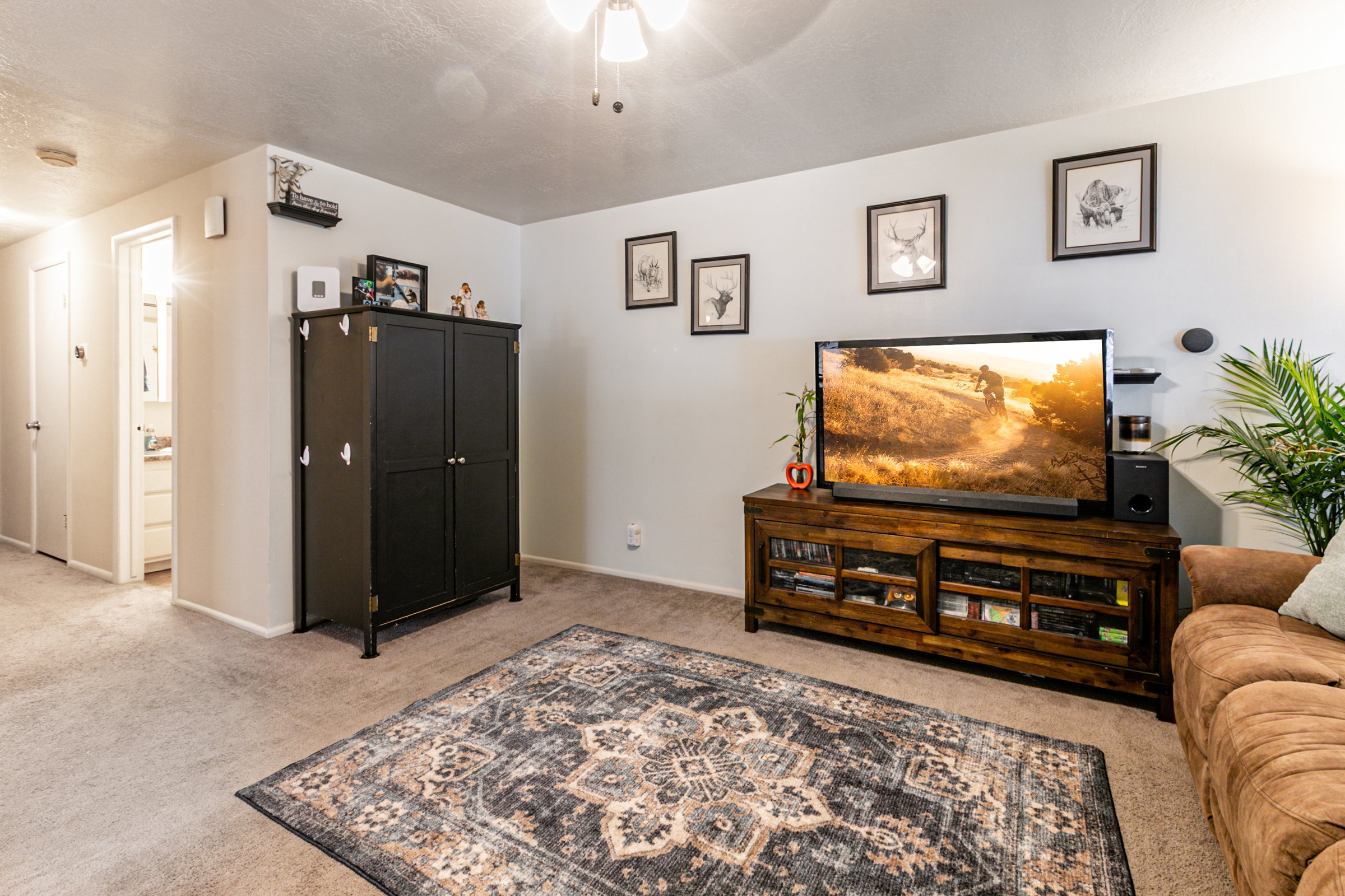 Carpeted living area featuring light neutral wall tones and a ceiling fan with integrated lighting