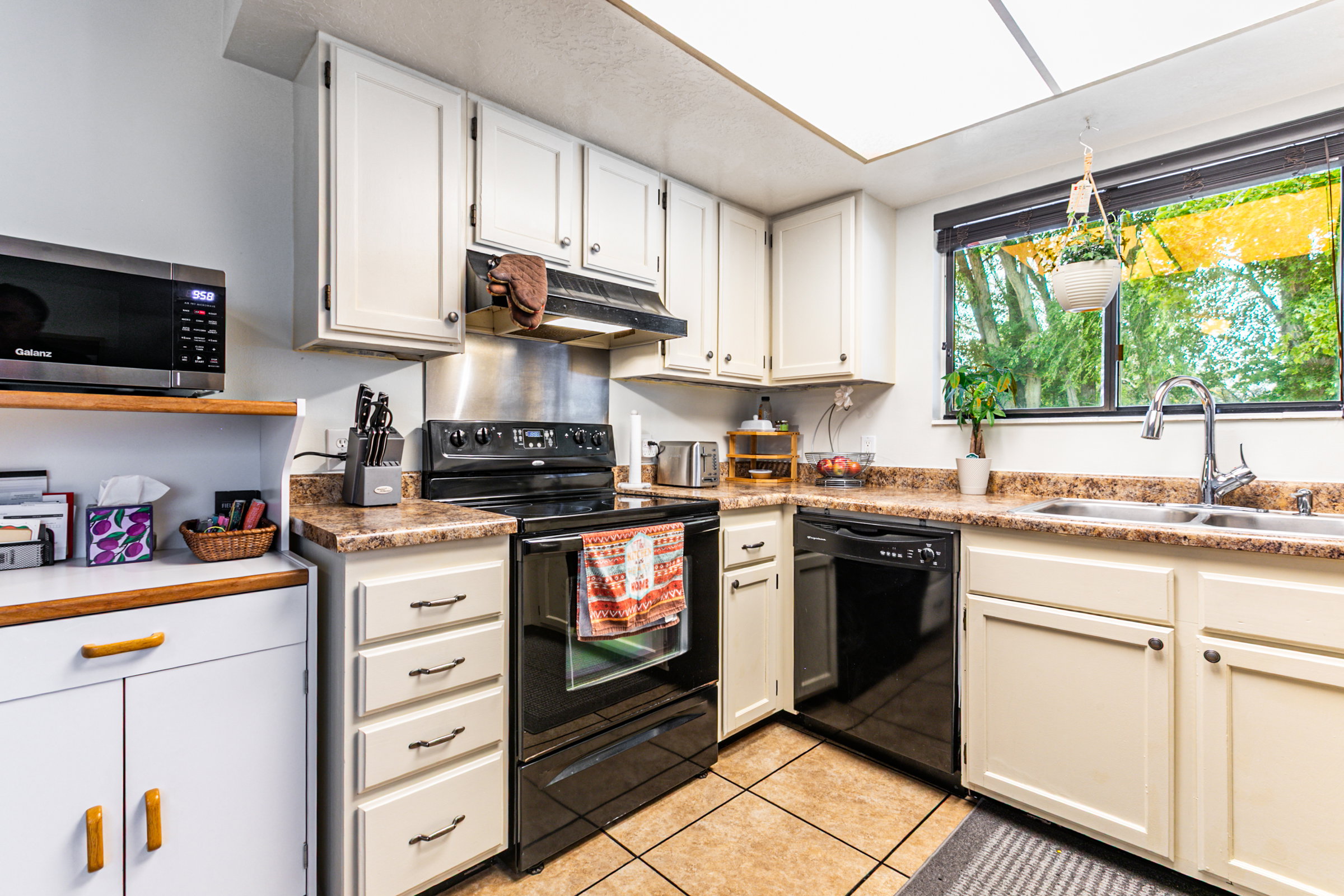 Kitchen with white cabinetry, black appliances, a double basin sink, and a window
