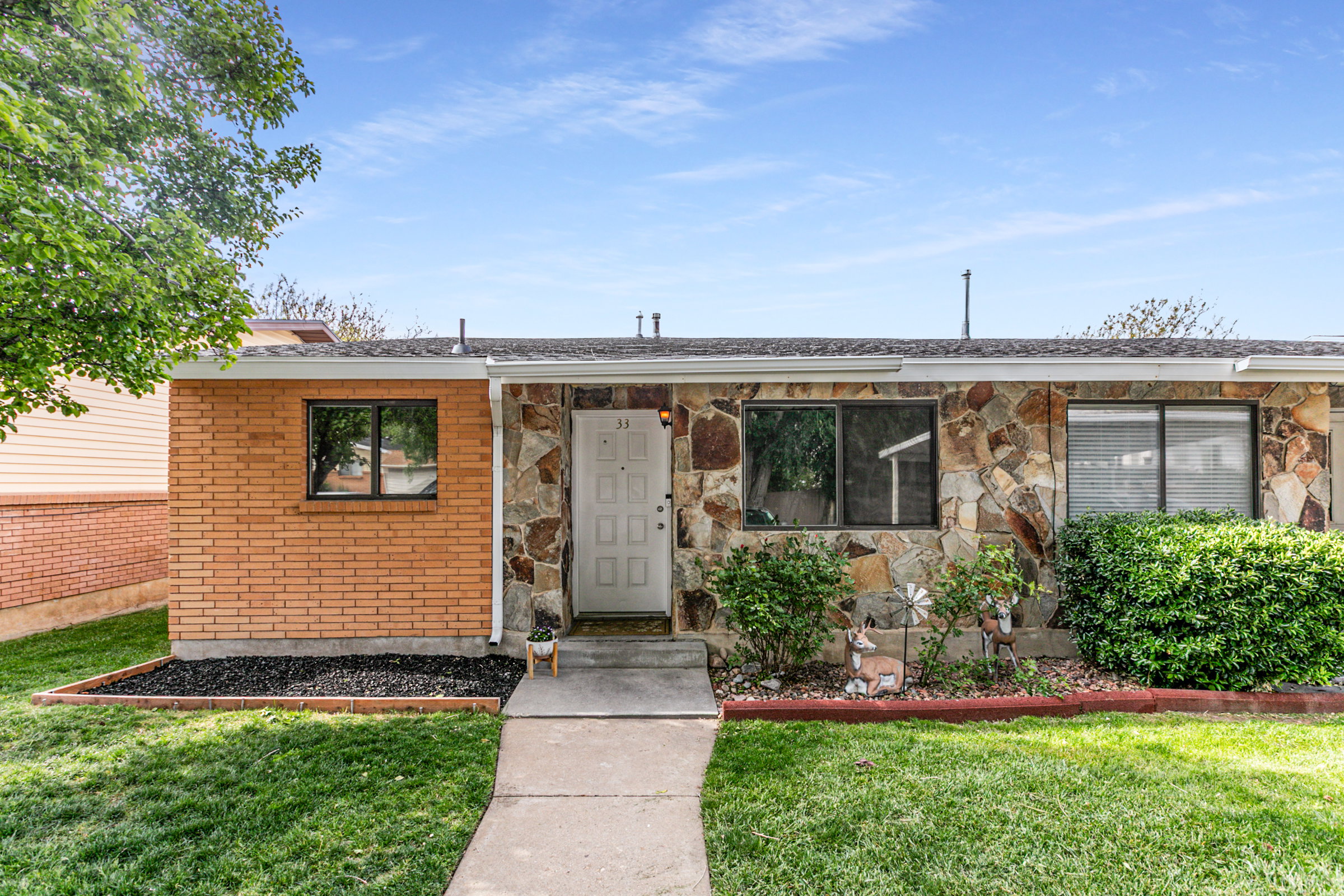 Exterior featuring a stone veneer facade, brick accent wall, white entry door, multiple windows, and a concrete walkway