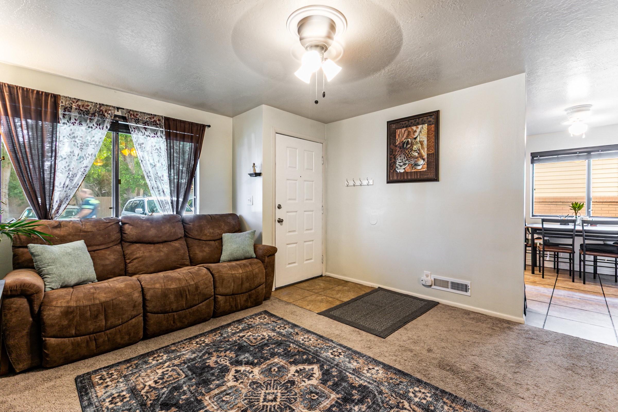 Living area featuring light-colored walls, carpet flooring, a front entry door with a multi-pane design, and a ceiling fan with integrated lighting