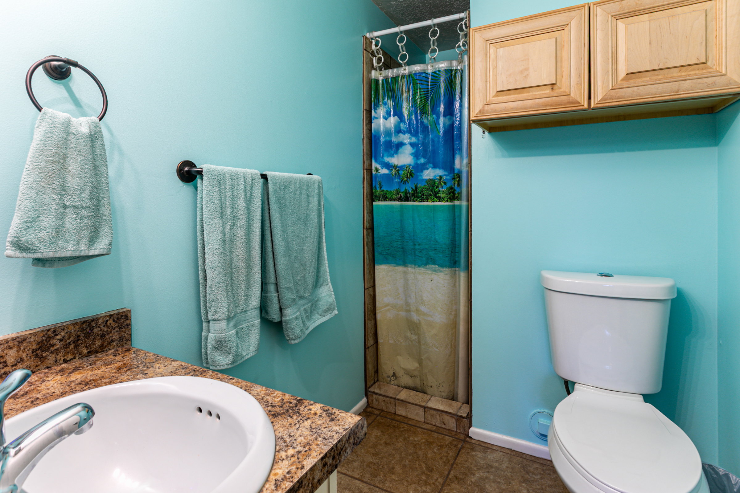 Bathroom featuring a single vanity with an integrated sink, a tiled shower, and overhead cabinetry