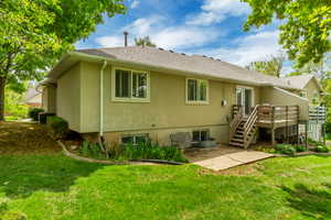 Rear stucco exterior featuring a multi-level deck with wooden railings, a sliding glass door, and a ground-level concrete patio