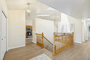 Open-concept landing area featuring wood-finish flooring, a wood balustrade staircase, high ceilings with skylights, and multiple decorative light fixtures