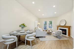 Vaulted ceilings highlight the open concept living and dining areas featuring wood-finish flooring, recessed lighting, a fireplace with a wood mantel, and French doors