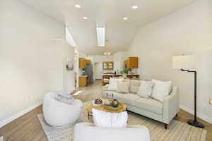 Open-concept living area featuring wood-finish flooring, vaulted ceilings, recessed lighting, and a skylight