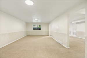 Open room featuring neutral-toned carpet, white painted walls, and textured wainscoting