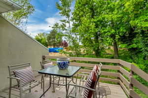 Private outdoor deck featuring a wood-finish railing, stucco-finish exterior wall, and surrounding mature trees