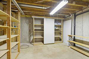 Unfinished basement featuring exposed joists, concrete foundation walls, and a concrete floor