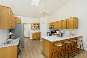 Kitchen featuring wood cabinetry, light-toned countertops, wood-finish flooring, a vaulted ceiling, and a skylight