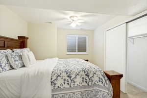 Bedroom featuring light-colored walls, a ceiling fan with integrated lighting, a window with horizontal blinds, and a built-in closet with sliding doors and shelving