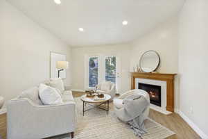 Living area featuring a fireplace with a wood mantel and tile surround, wood-finish flooring, recessed lighting, and a double-door exterior entry