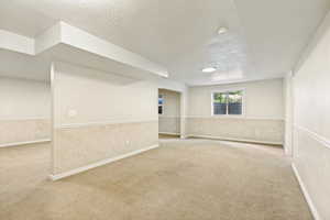 Spacious room featuring neutral carpeting, light-toned walls with wainscoting, a flush-mount ceiling light, and a window providing natural illumination