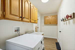 Dedicated laundry area featuring abundant wood cabinetry, integrated laundry hookups, a functional countertop, and wood-finish flooring