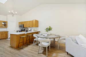 Open-concept kitchen and dining area featuring wood-finish flooring, vaulted ceilings, and a kitchen island with seating