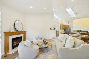 Living area featuring a fireplace with a wood mantel and tile surround, wood-finish flooring, vaulted ceilings, recessed lighting, and skylights