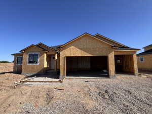 Under-construction single-story residence with a two-car garage and gabled rooflines, featuring dark shingles and framed windows