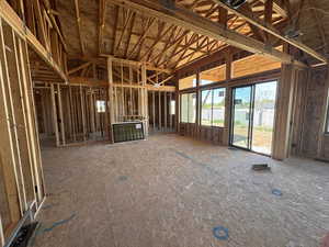 New construction framing featuring an open floorplan, high vaulted ceilings with exposed beams, and extensive rear-facing windows and sliding glass doors