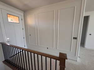 Entryway featuring a white paneled door with a rectangular window, decorative wall molding, and a staircase with a wood-finish handrail and black balusters