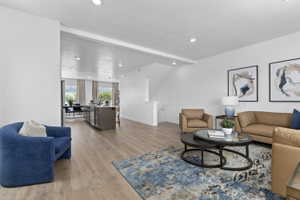Open-concept living area featuring wood-finish flooring, recessed lighting, white walls, and a staircase with white balusters