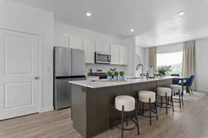 Open-concept kitchen featuring an expansive island with seating, stainless steel appliances, white upper cabinetry, and wood-finish flooring