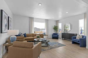 Spacious living area featuring light wood-finish flooring, recessed lighting, and large windows with vertical blinds