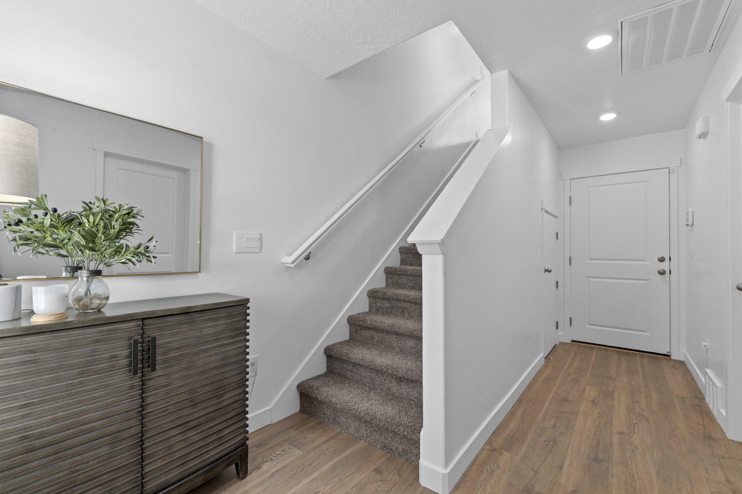Entryway featuring wood-finish flooring, a carpeted staircase with a white handrail, recessed lighting, and a white paneled door