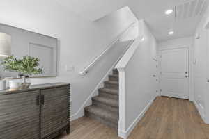 Entryway featuring wood-finish flooring, a carpeted staircase with a white handrail, recessed lighting, and a white paneled door