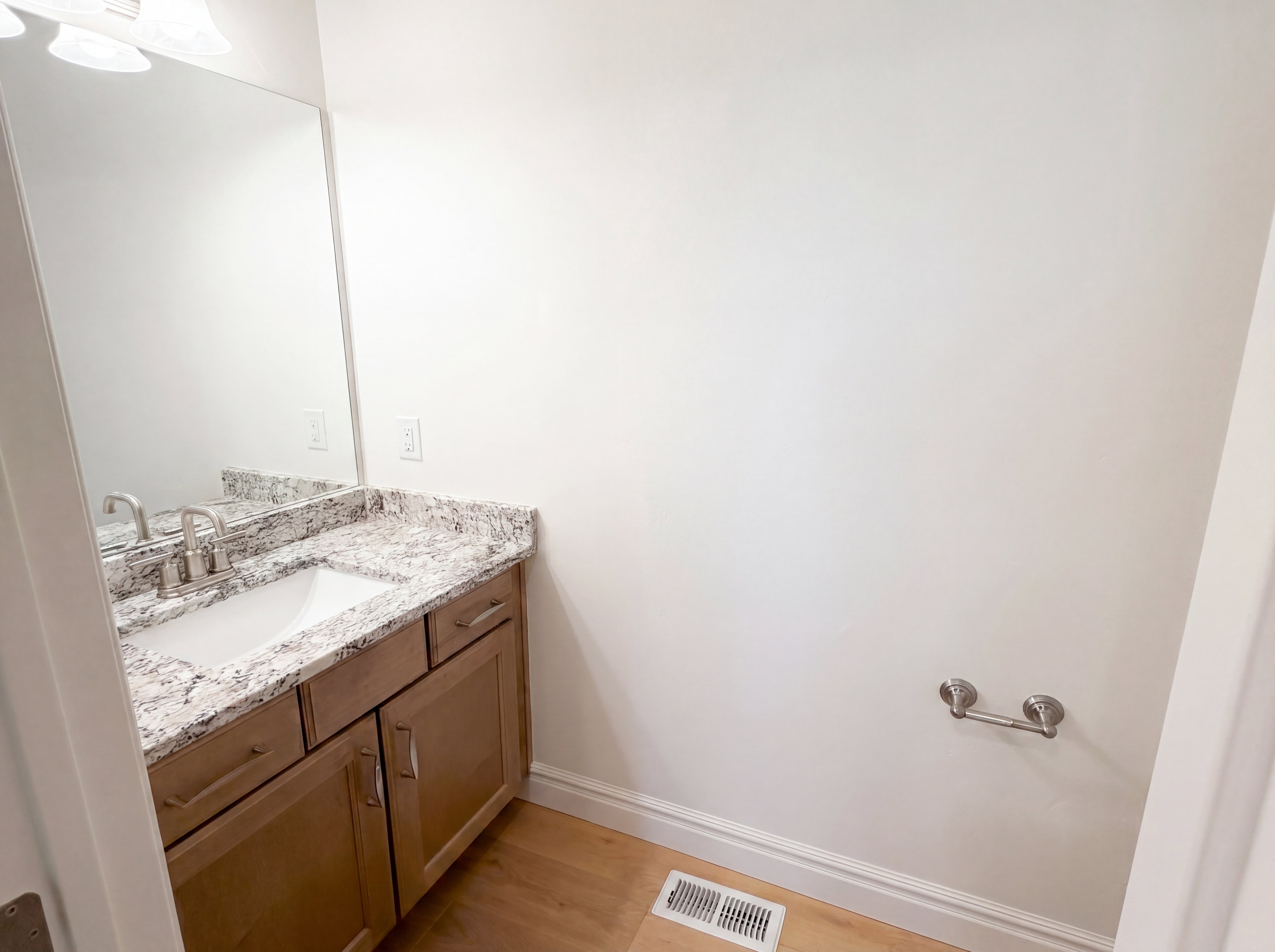 Bathroom vanity with a light-toned wood-finish cabinet, a white sink, and a speckled countertop