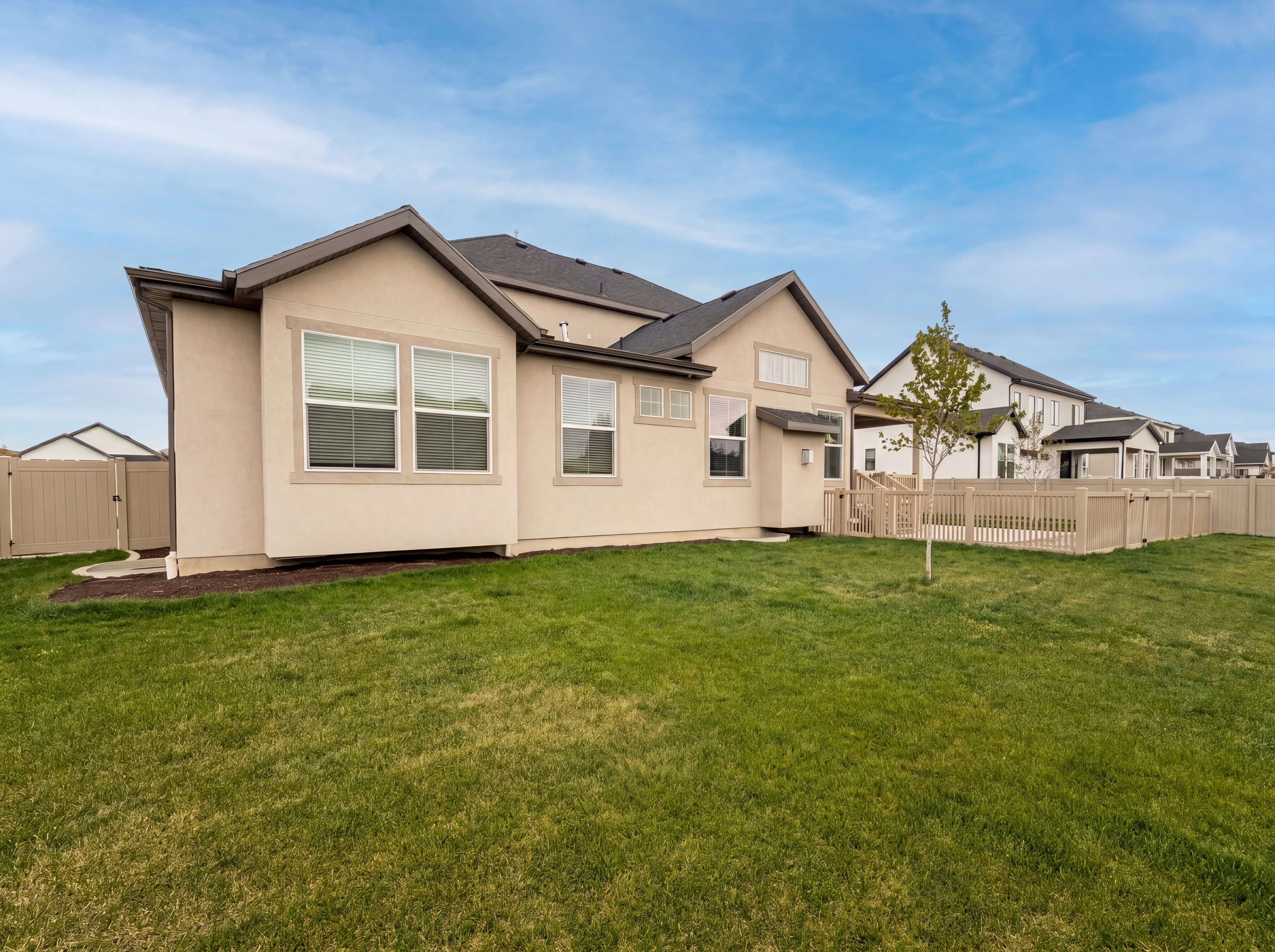 Expansive green lawn bordering the property, featuring a beige privacy fence and a young deciduous tree