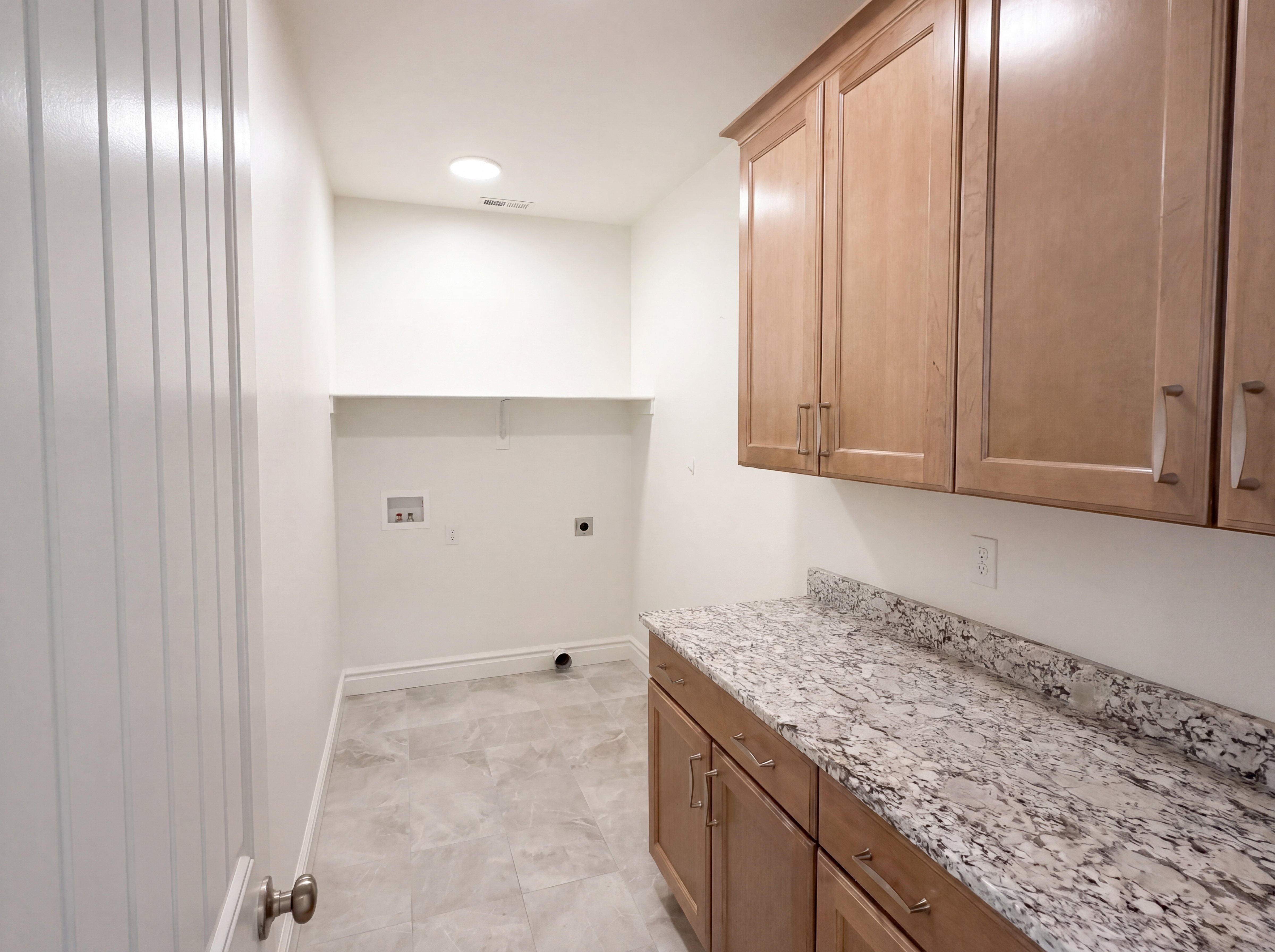 Utility room featuring light wood-finish cabinetry, a granite-patterned countertop, and neutral tile flooring
