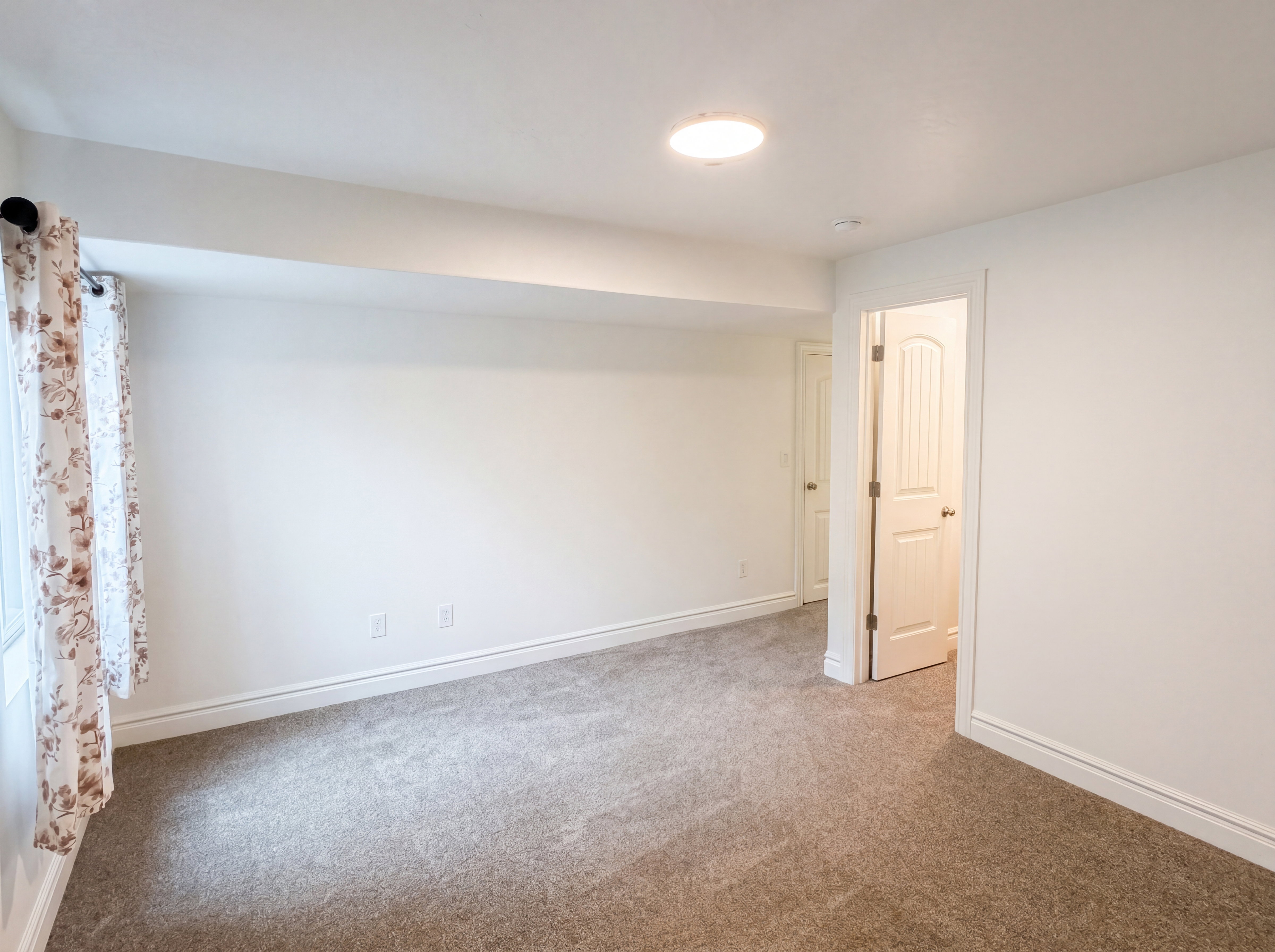 Spacious room featuring neutral carpeting, white walls, recessed lighting, and a window with a curtain rod