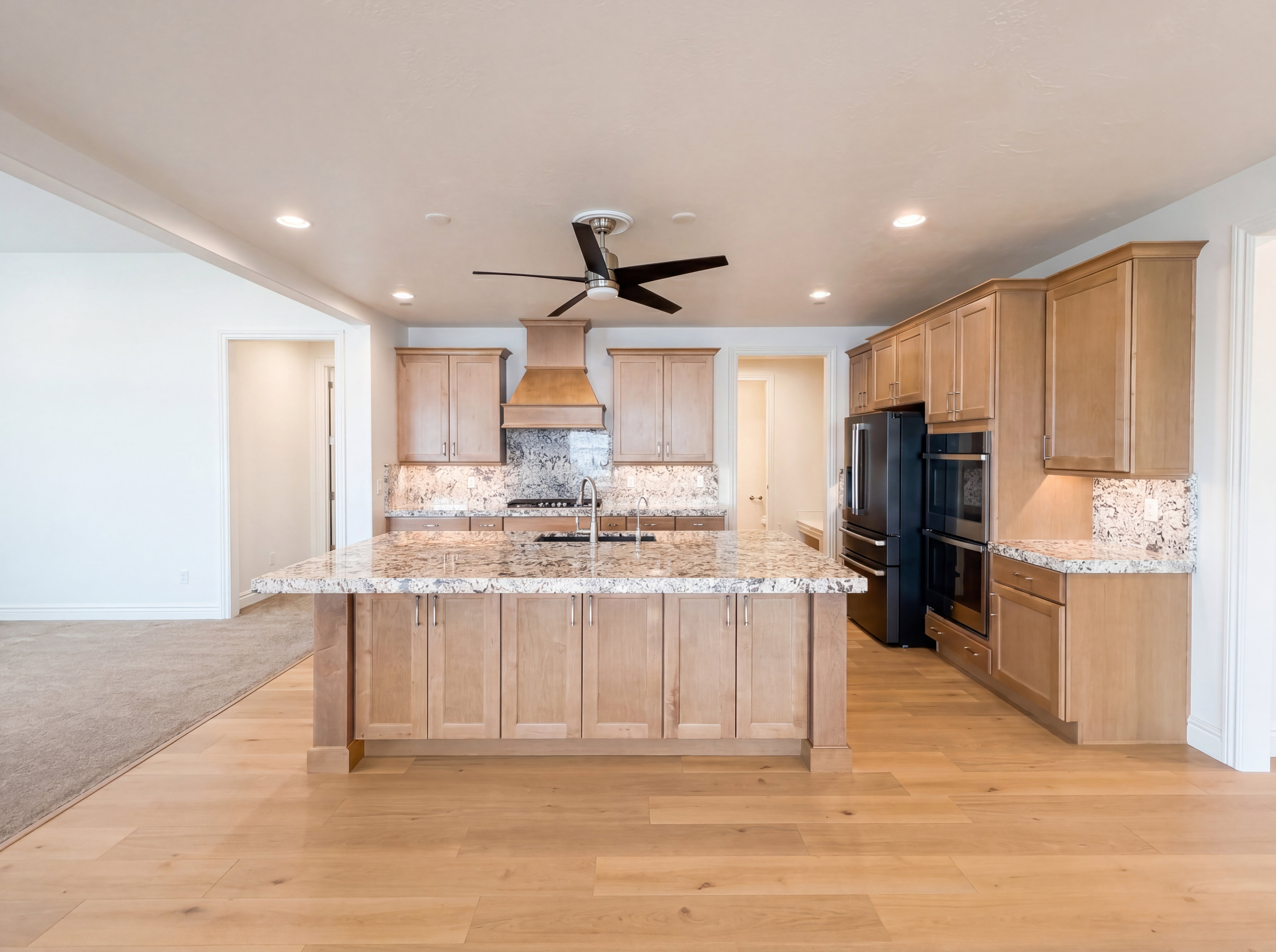 Expansive kitchen featuring light wood-finish cabinetry, granite countertops, and a substantial island with a stainless steel sink
