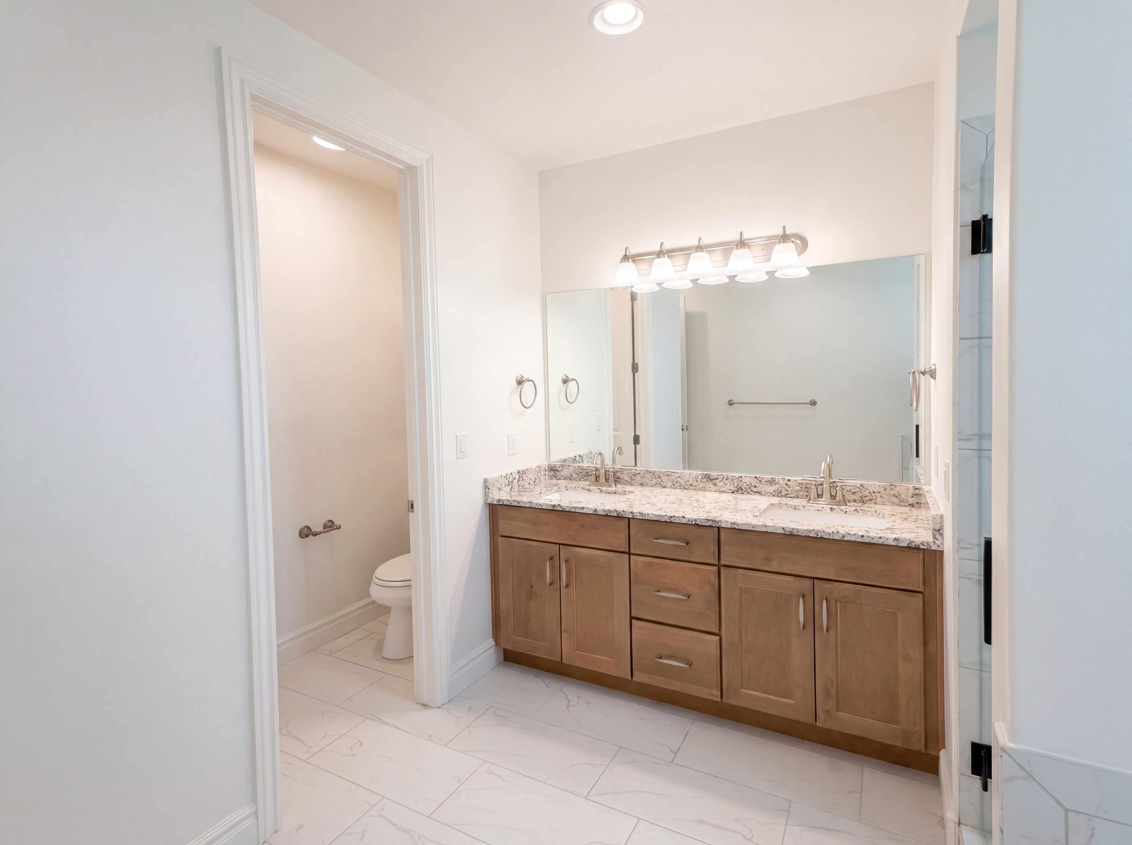 Double vanity with light wood-finish cabinetry and granite-style countertop