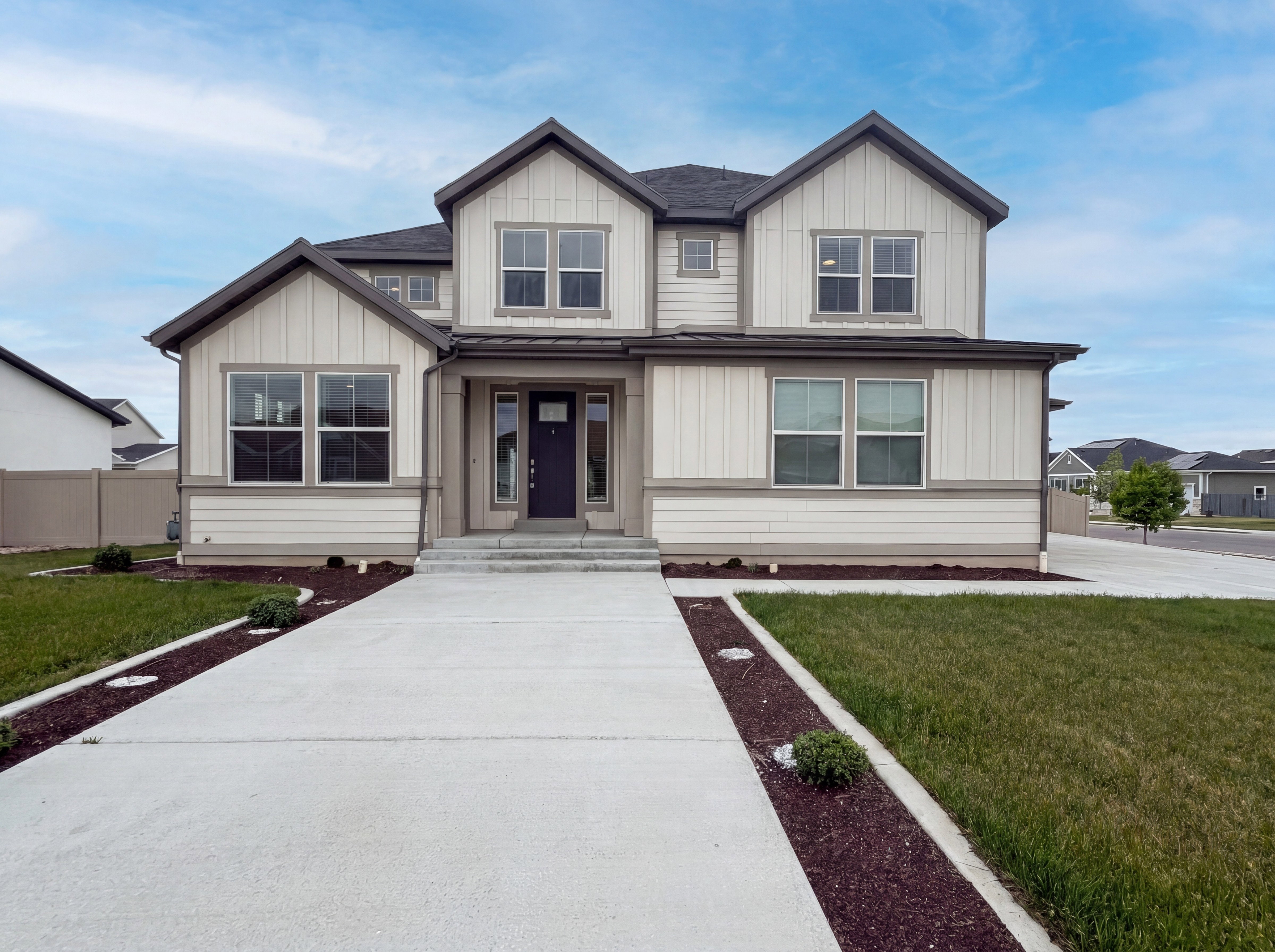 Contemporary two-story residence featuring a dark gray roof, light siding with vertical board and batten accents, a dark entry door, and multiple large windows