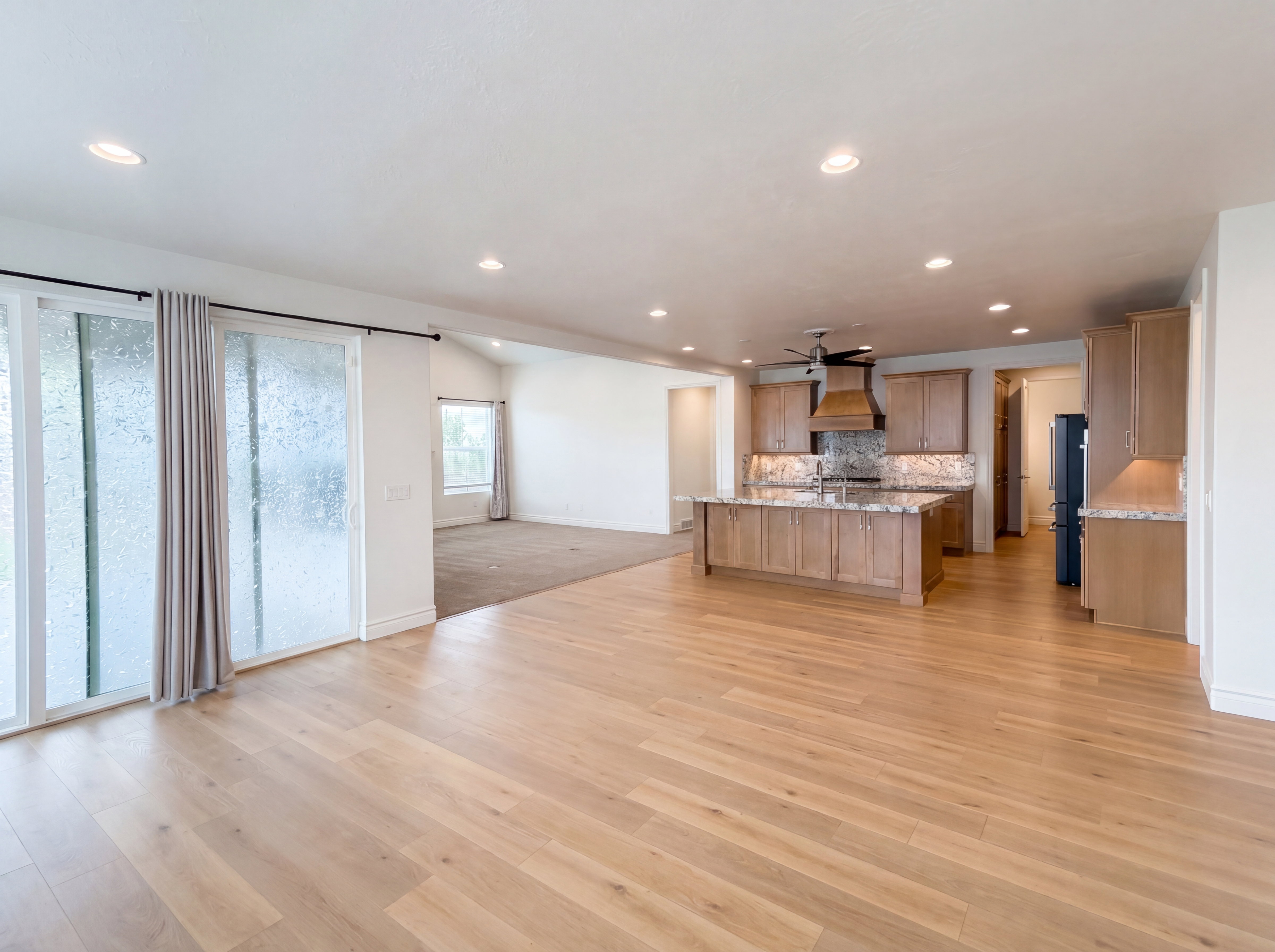 Expansive open-concept living space featuring light wood-finish flooring, recessed lighting, and a modern kitchen