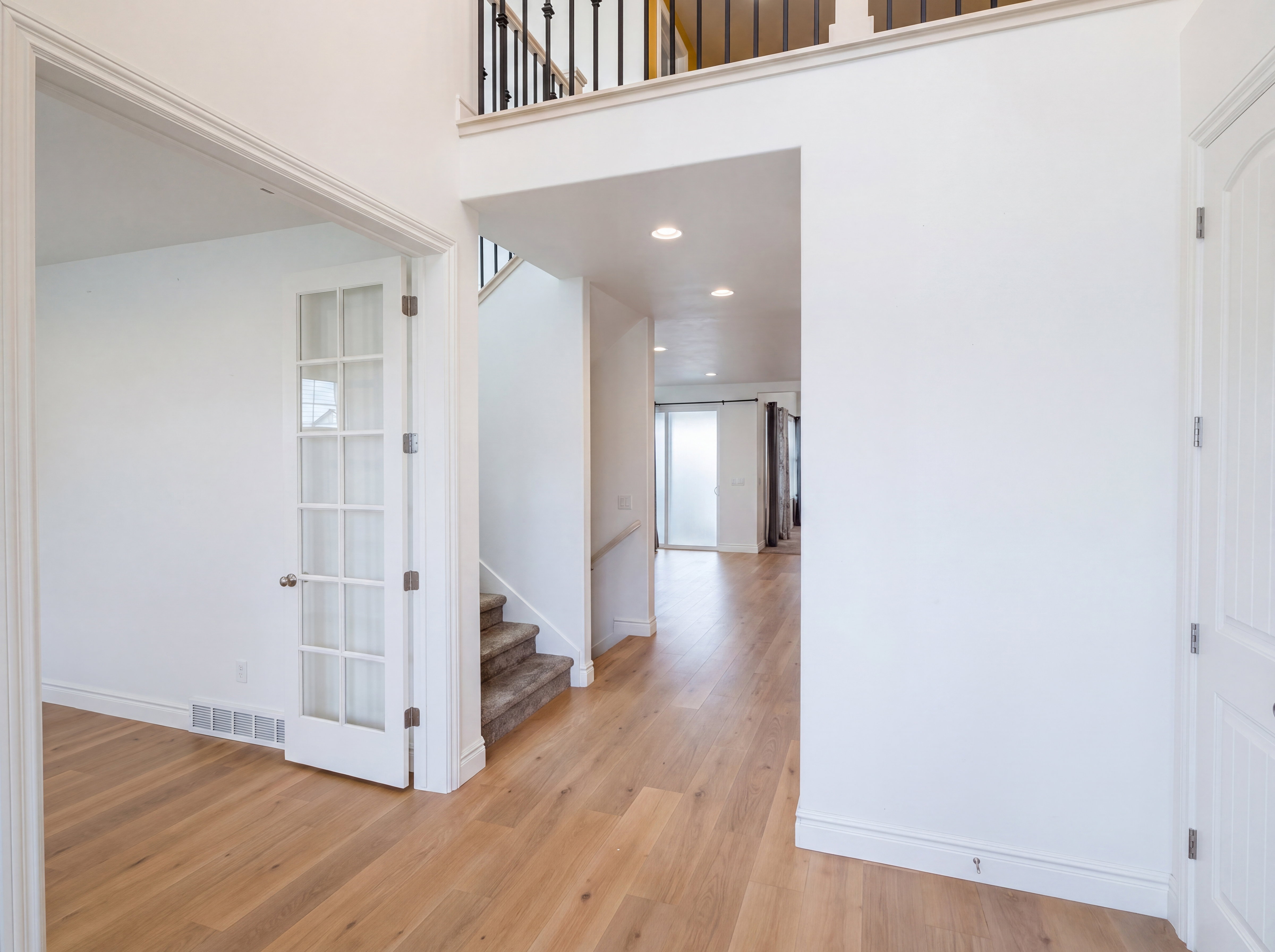 Foyer featuring wood-finish flooring, a white paneled door, and a staircase with a wrought iron railing