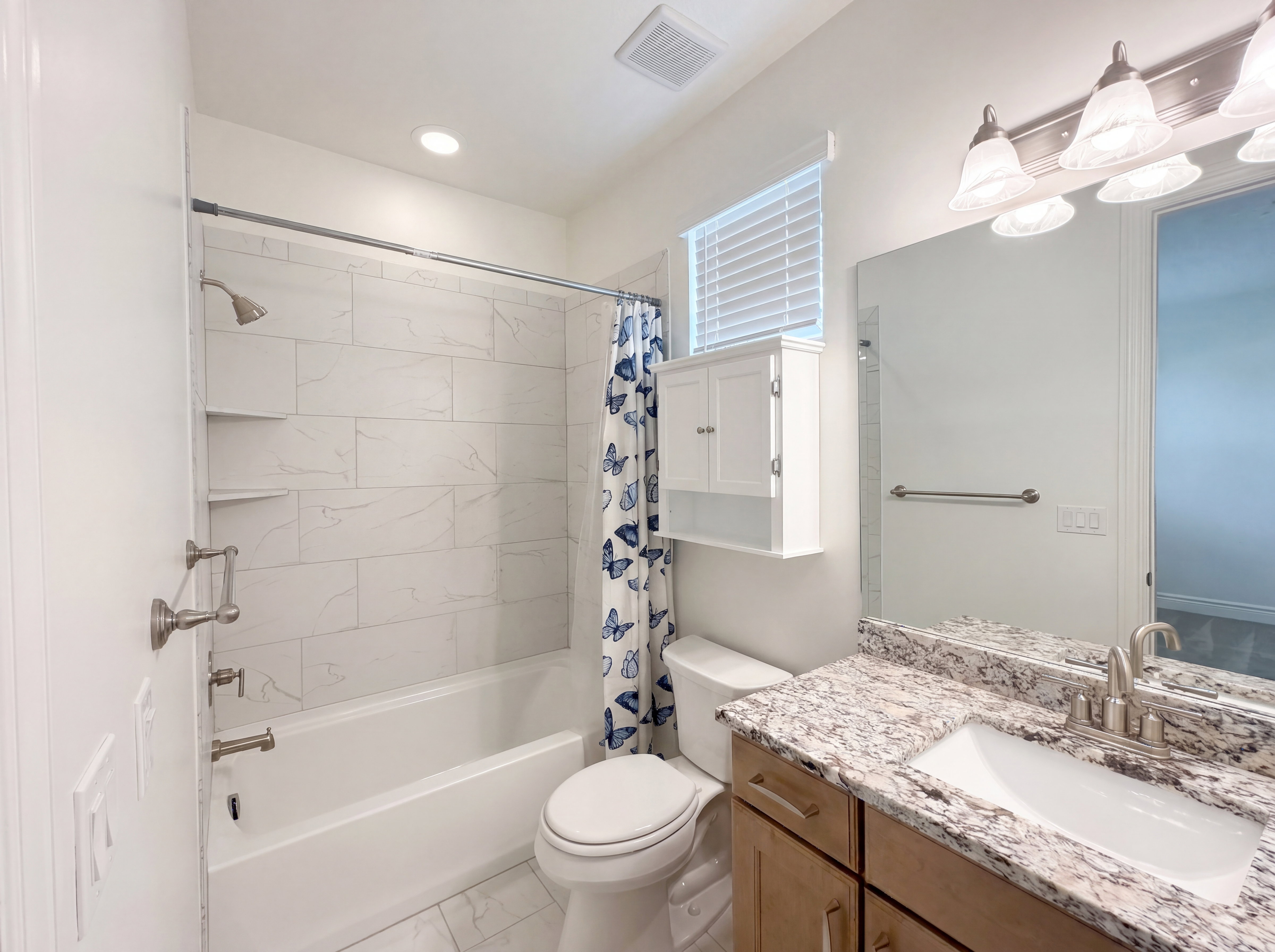 Full bathroom featuring a tub and shower combination with white subway-style tile surround and integrated shelving, a single vanity with a granite countertop and undermount sink, and a wall-mounted medicine cabinet