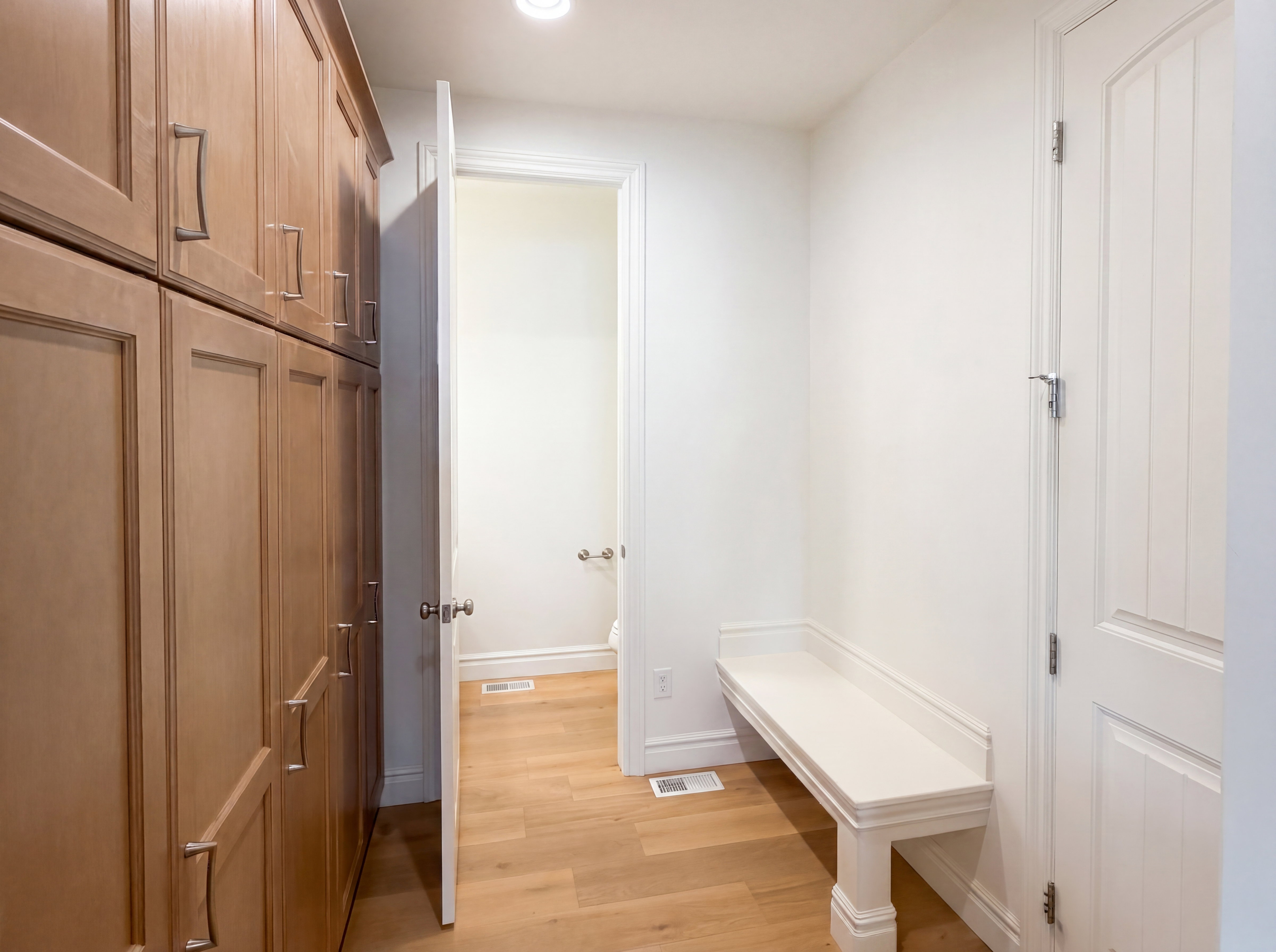 Custom wood cabinetry with brushed nickel hardware, wood-finish flooring, recessed lighting, and a built-in white bench