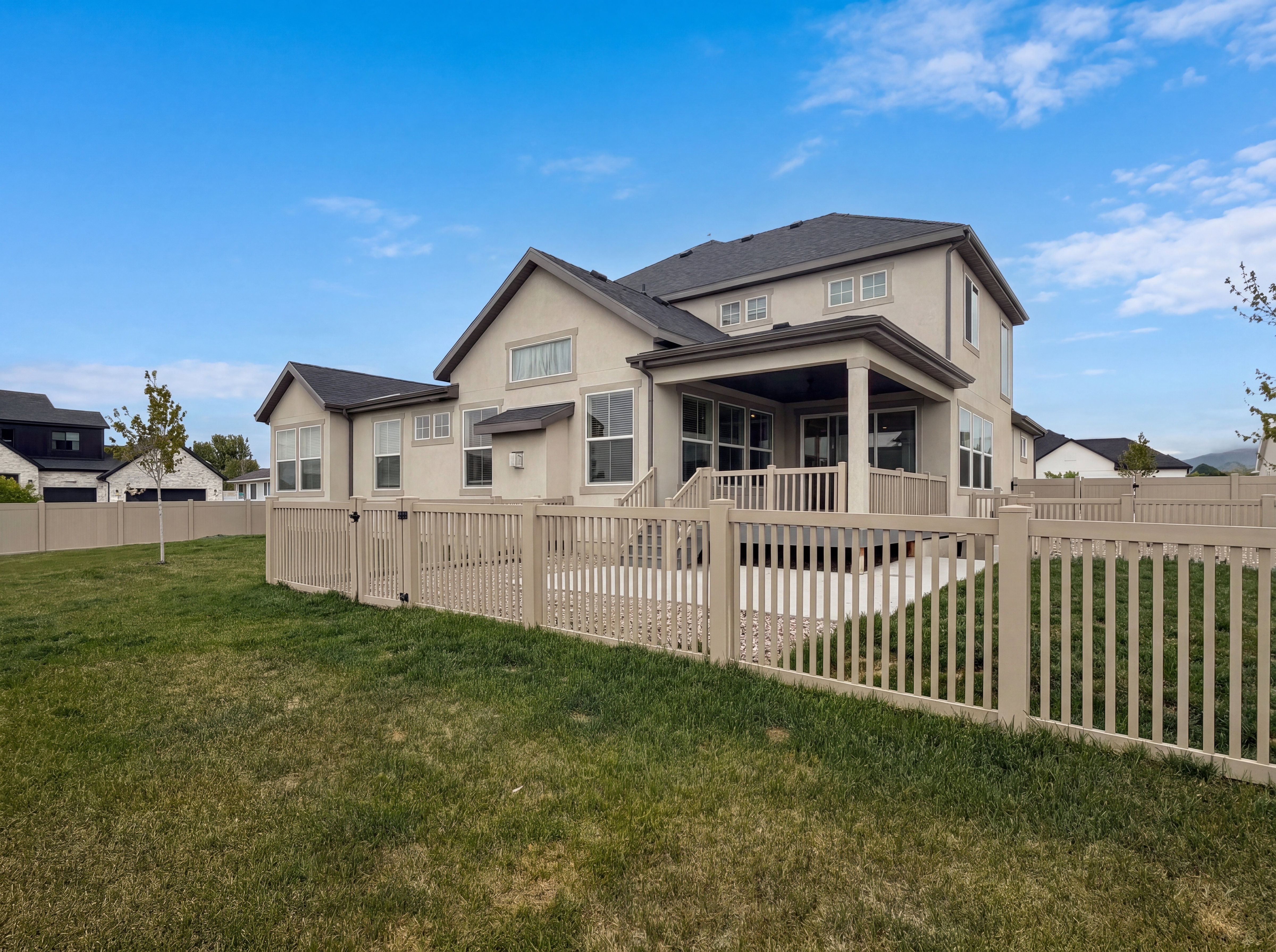 Expansive backyard featuring a manicured lawn, full perimeter fencing, and a covered patio with a deck