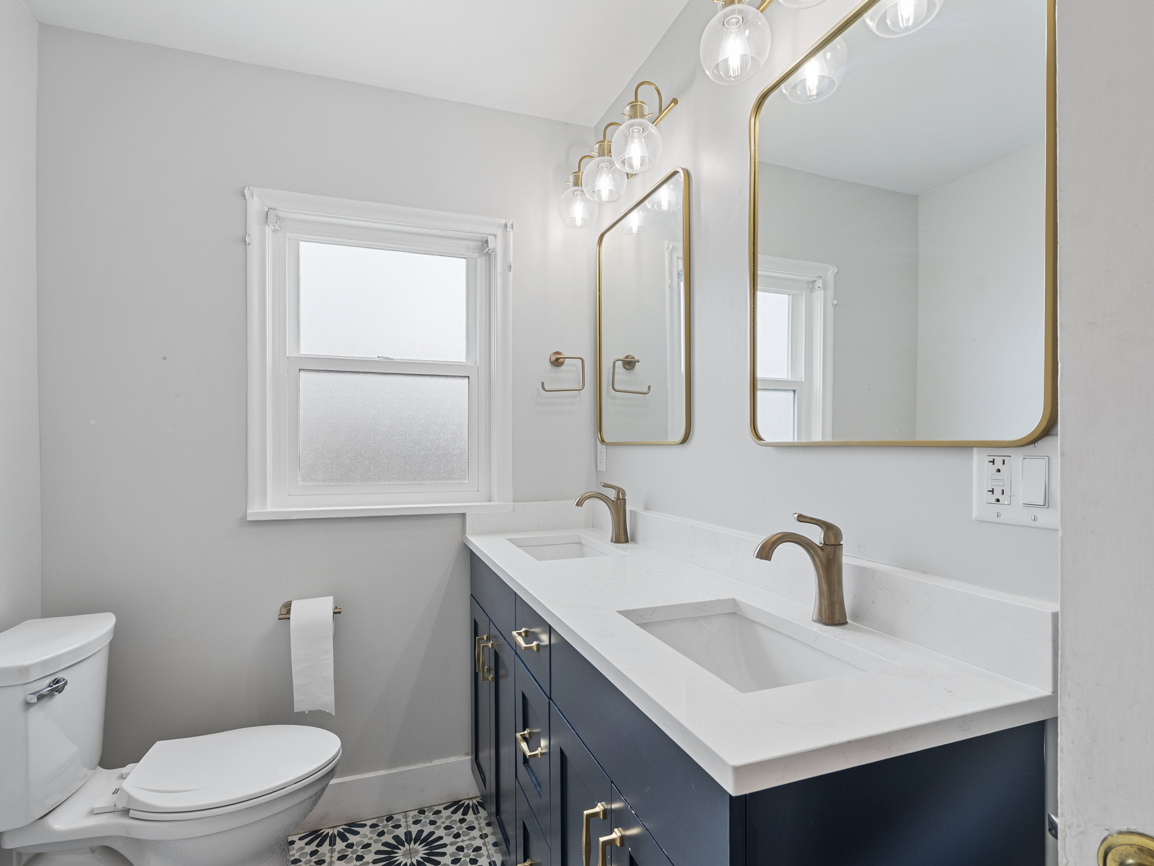 Bathroom featuring a dual sink vanity with a white countertop, two gold-framed rectangular mirrors, and a multi-bulb light fixture