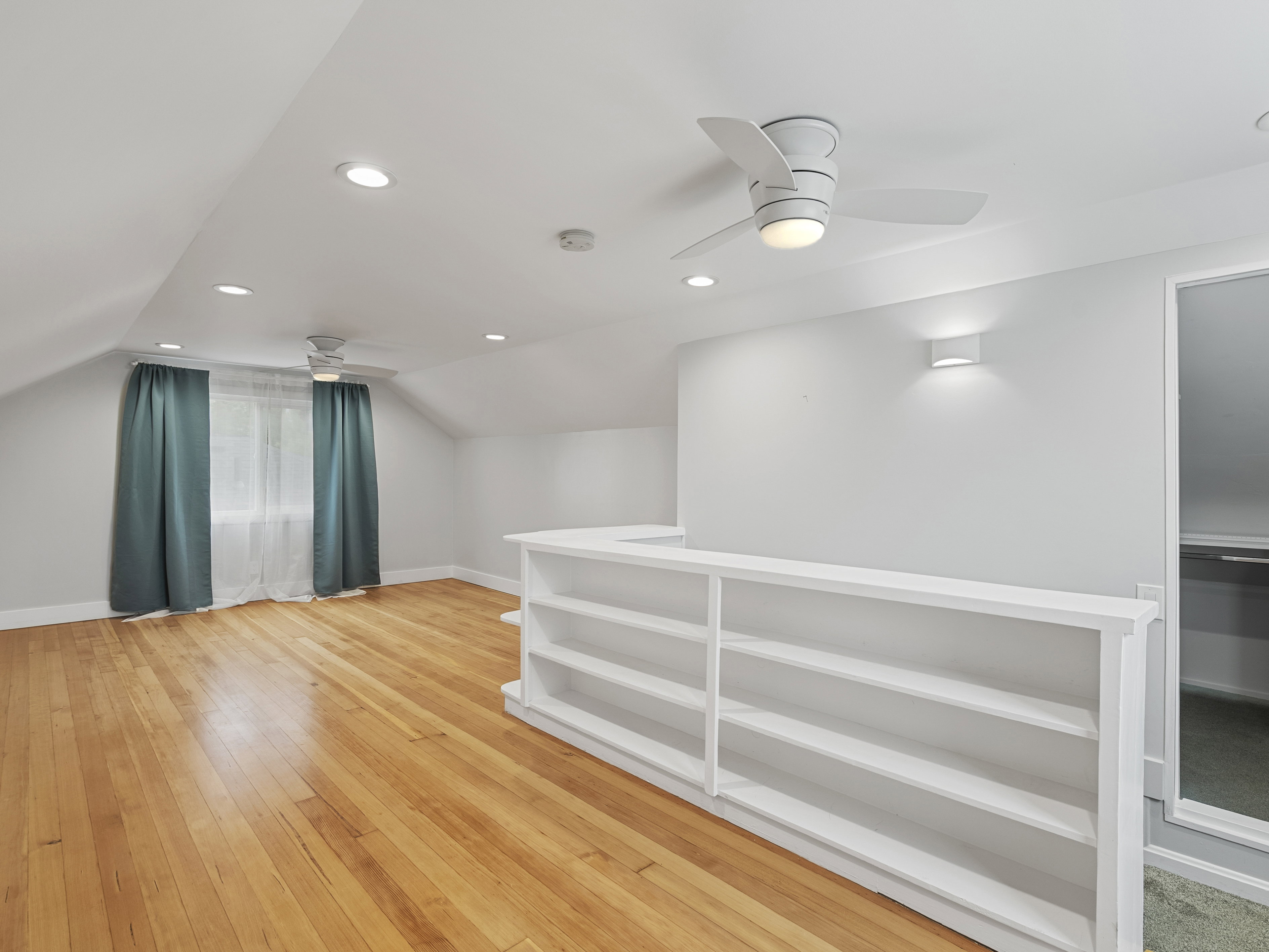 Upper-level loft space featuring wood-finish flooring, a contemporary ceiling fan, recessed lighting, and built-in shelving
