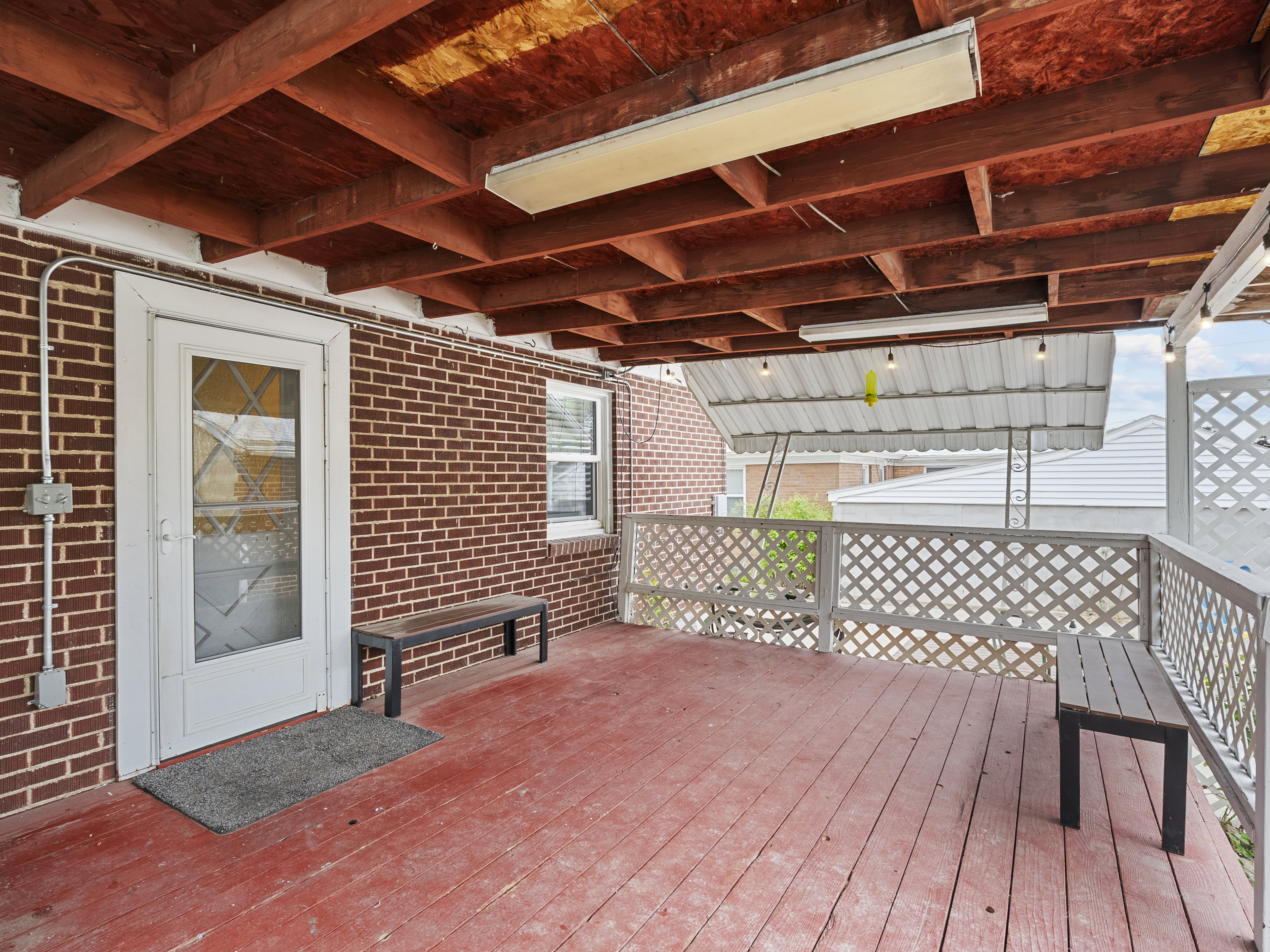 Covered deck with a red wood-finish floor and exposed wood beam ceiling