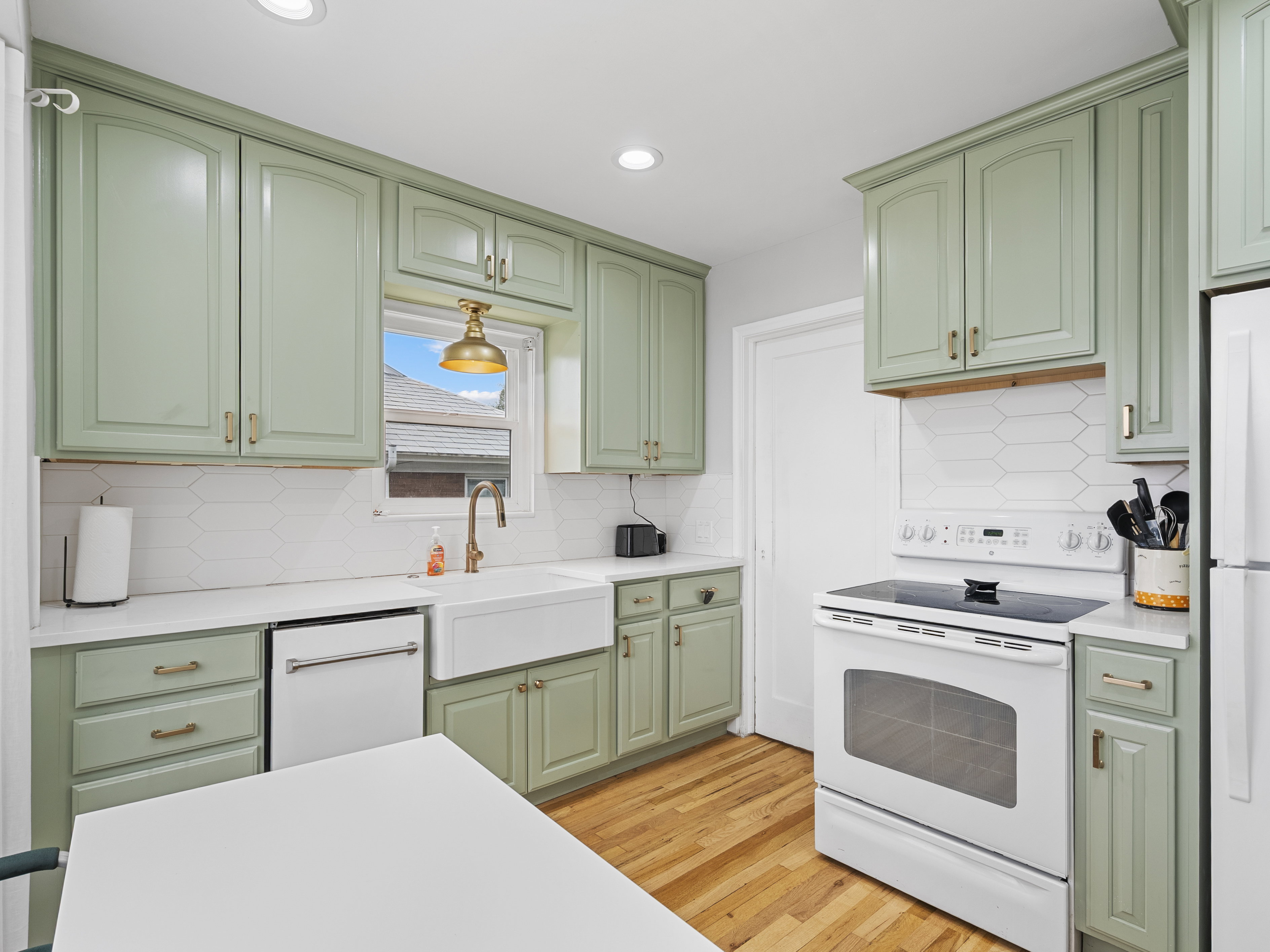 Kitchen featuring sage green cabinetry, white countertops, wood-finish flooring, a farmhouse sink with a gooseneck faucet, and white subway tile backsplash