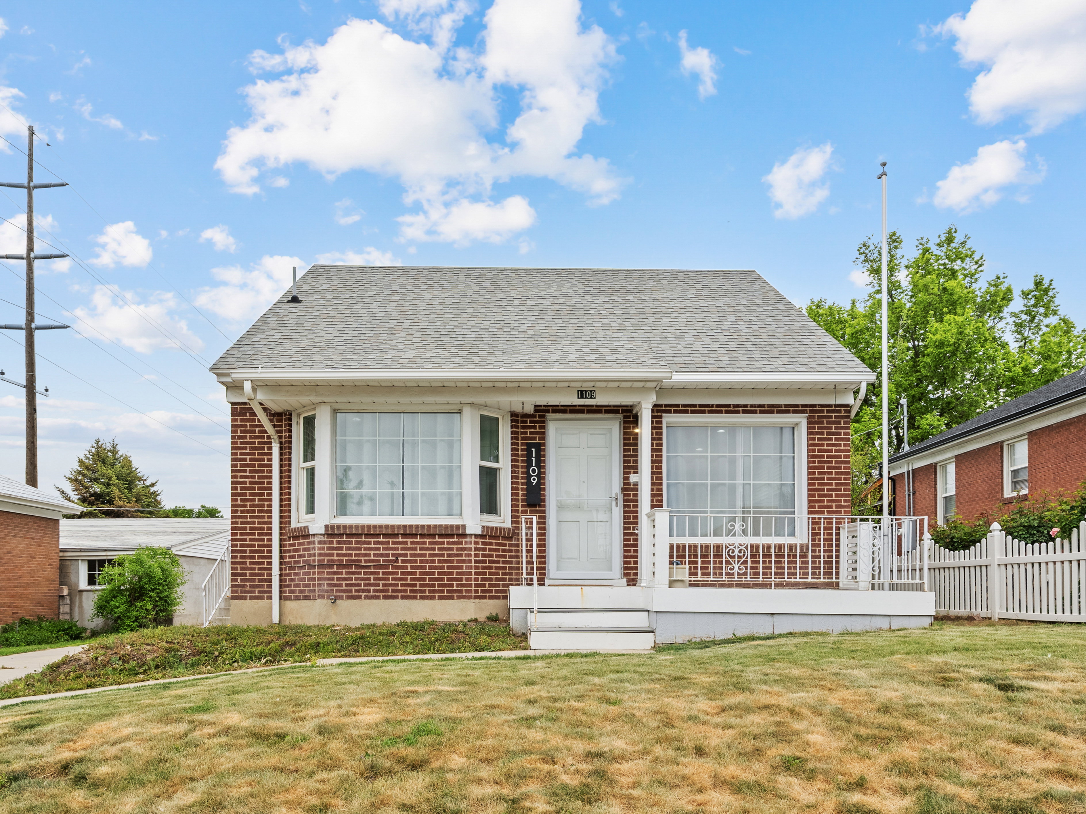 Brick exterior residence featuring a front porch with white railing, a white front door, and a traditional asphalt shingle roof
