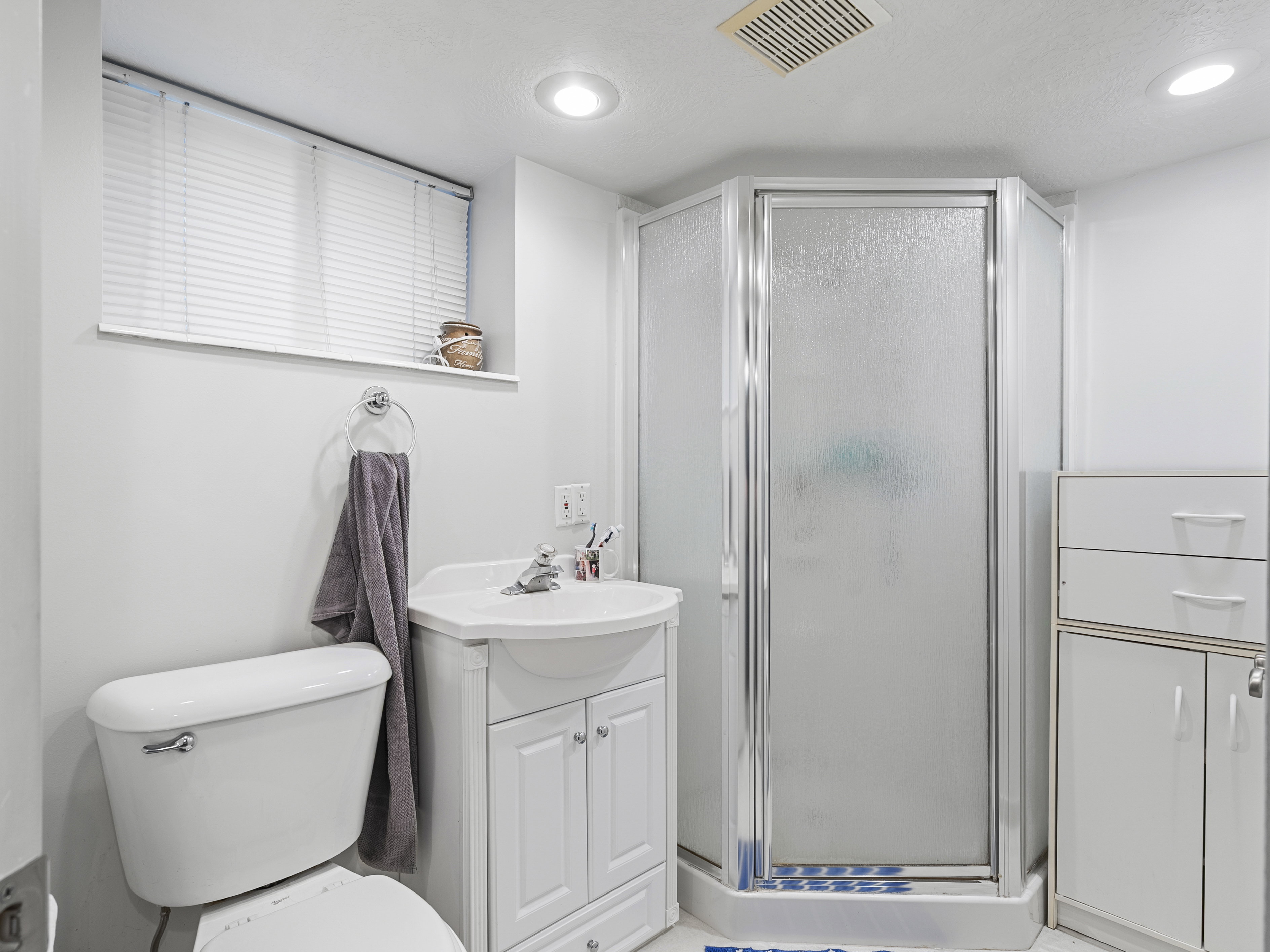 Bathroom featuring a corner shower with a frosted glass enclosure, white vanity with integrated sink, white toilet, and recessed lighting