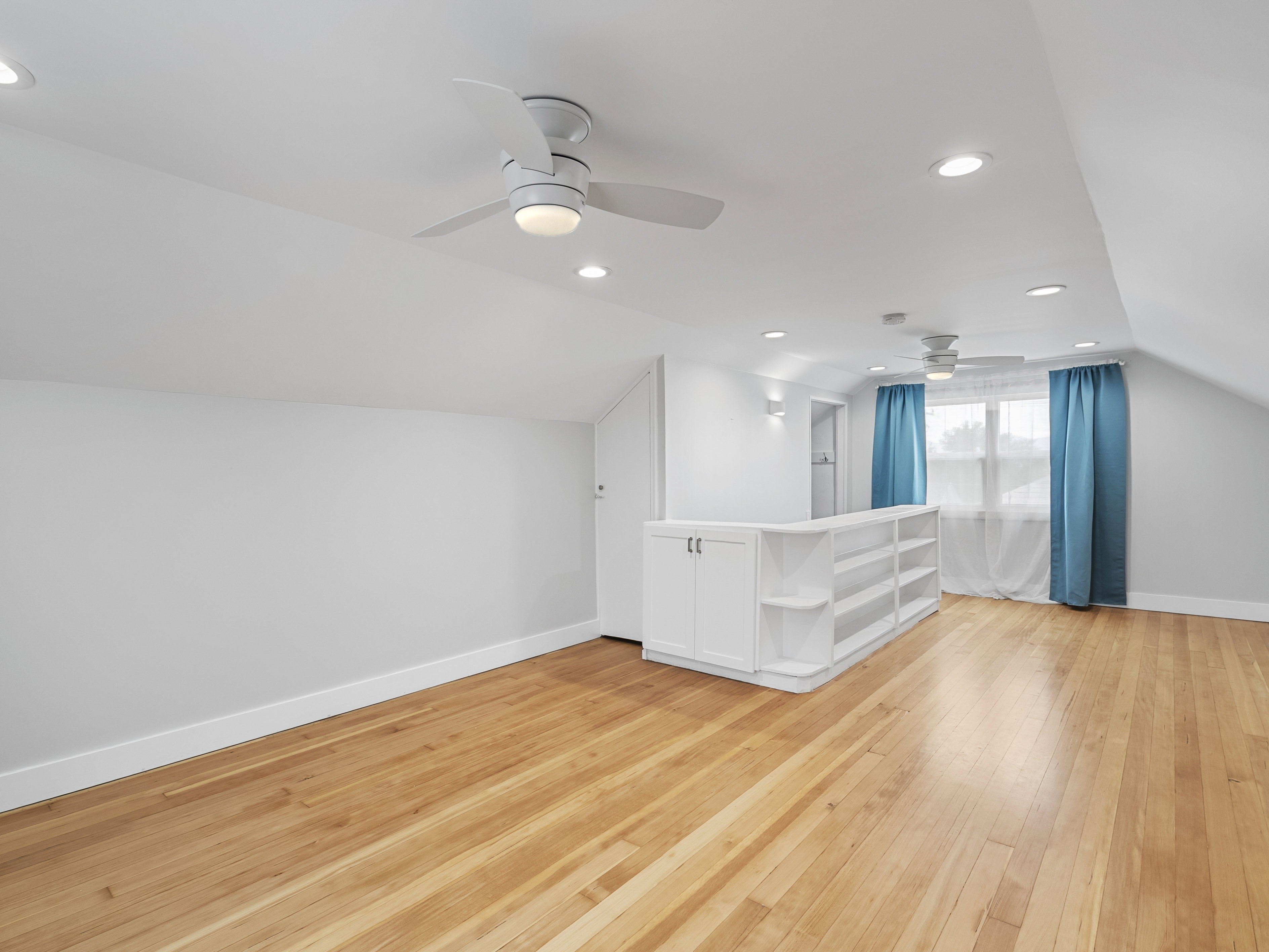 Spacious attic room featuring wood-finish flooring, recessed lighting, and multiple ceiling fans